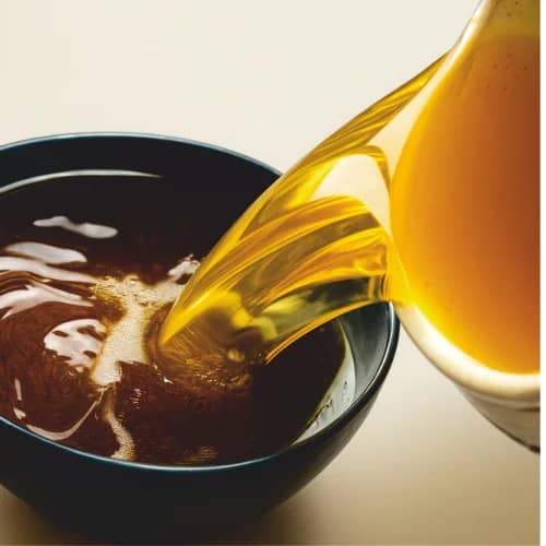 Golden palm kernel oil poured into a bowl beside palm kernels
