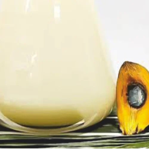 Pale solid palm stearin fraction in a container beside palm fruit